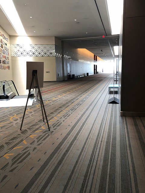 This hallway is completely carpeted in a pattern of light blue and gray stripes. On the left in this photo is an escalator that leads down to the Meeting Room level.
