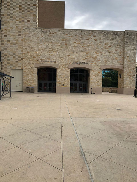 This photo shows a beige cement landing, leading up to a beige stone wall with three dark entryways. The entry on the leftmost side has text above it reading Lila Cockrell Theatre. The middle entry has text above reading Henry B. González Convention Center. The rightmost entry leads to a side outdoor porch and stairs to the River level.
