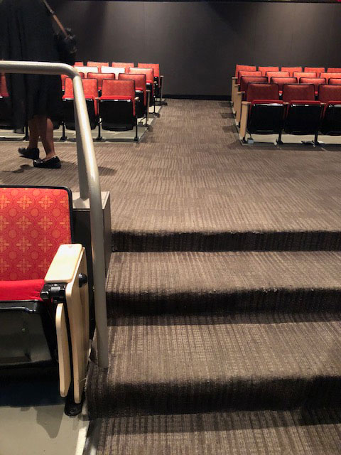 This photo shows the three steps in the aisle of the Lila Cockrell Theatre on the orchestra level. The carpet in the aisle is gray with lighter gray stripes.