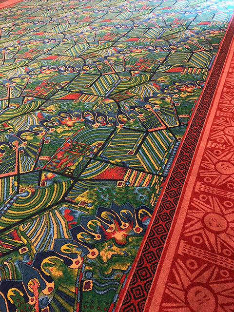 The carpet is a unique pattern of greens, yellows, and reds, all outlined by a red border.