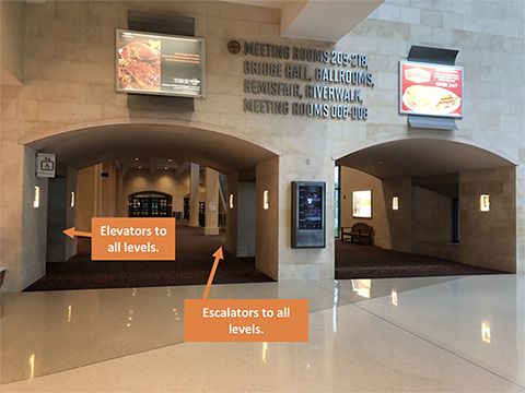 This photo shows two large archways leading to a hallway. The hallway contains elevators on the left and escalators further down the hall and slightly to the right.